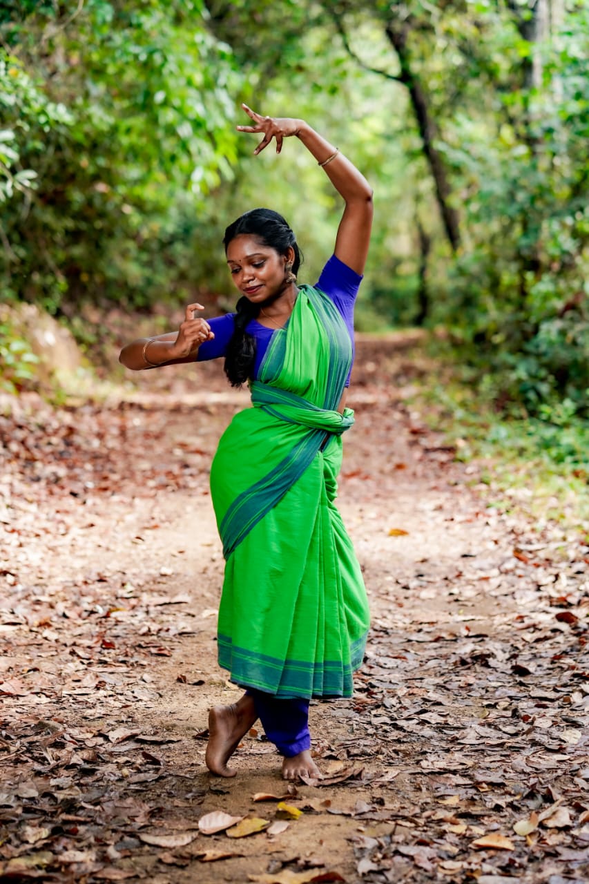 Lakshmi Kumaran in a classical dance pose on a leaf-strewn forest path