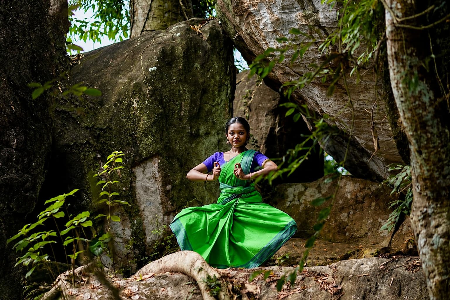 Lakshmi Kumaran in aramandi pose framed by moss-covered boulders