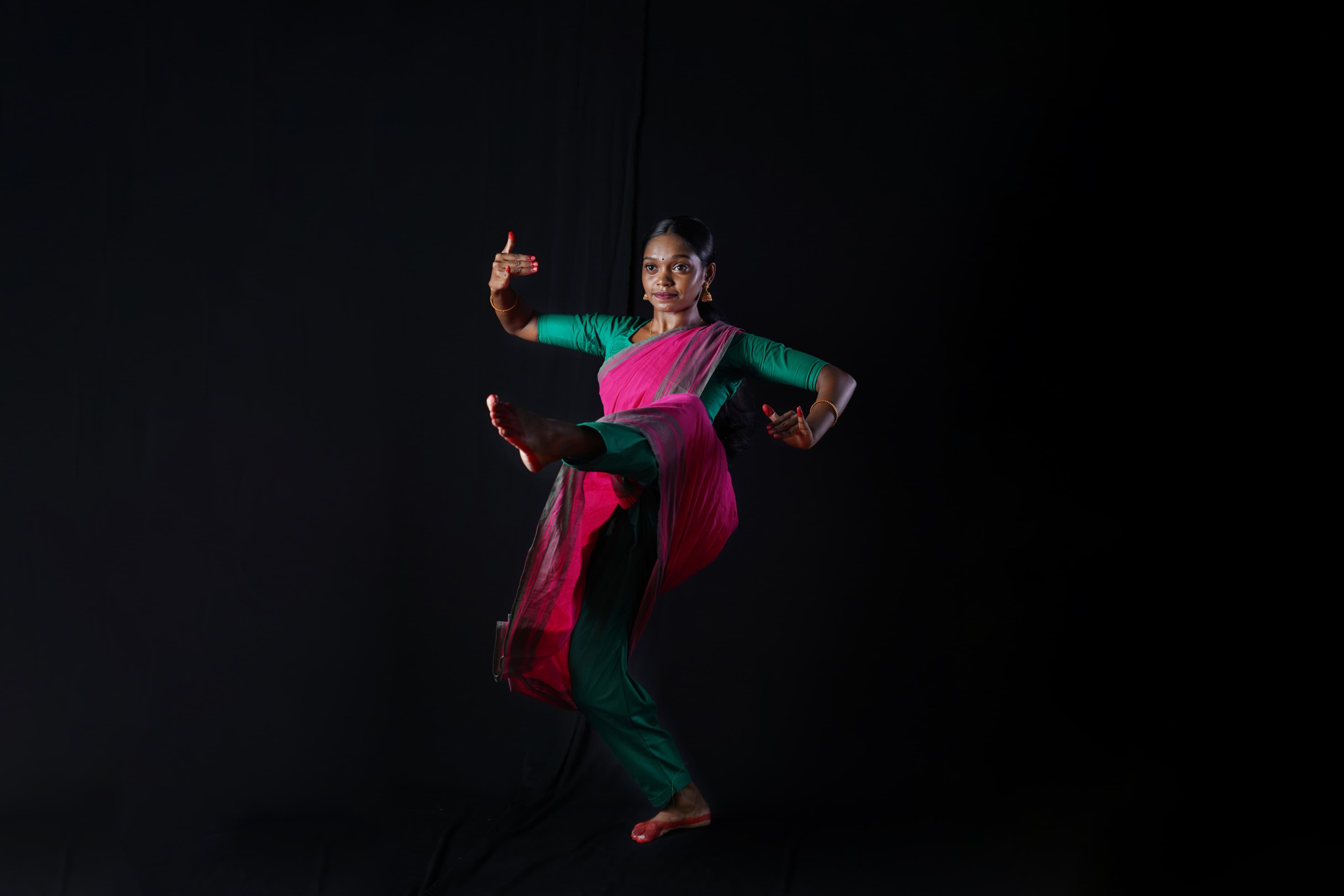 Lakshmi Kumaran performing a dynamic classical dance pose against a black backdrop