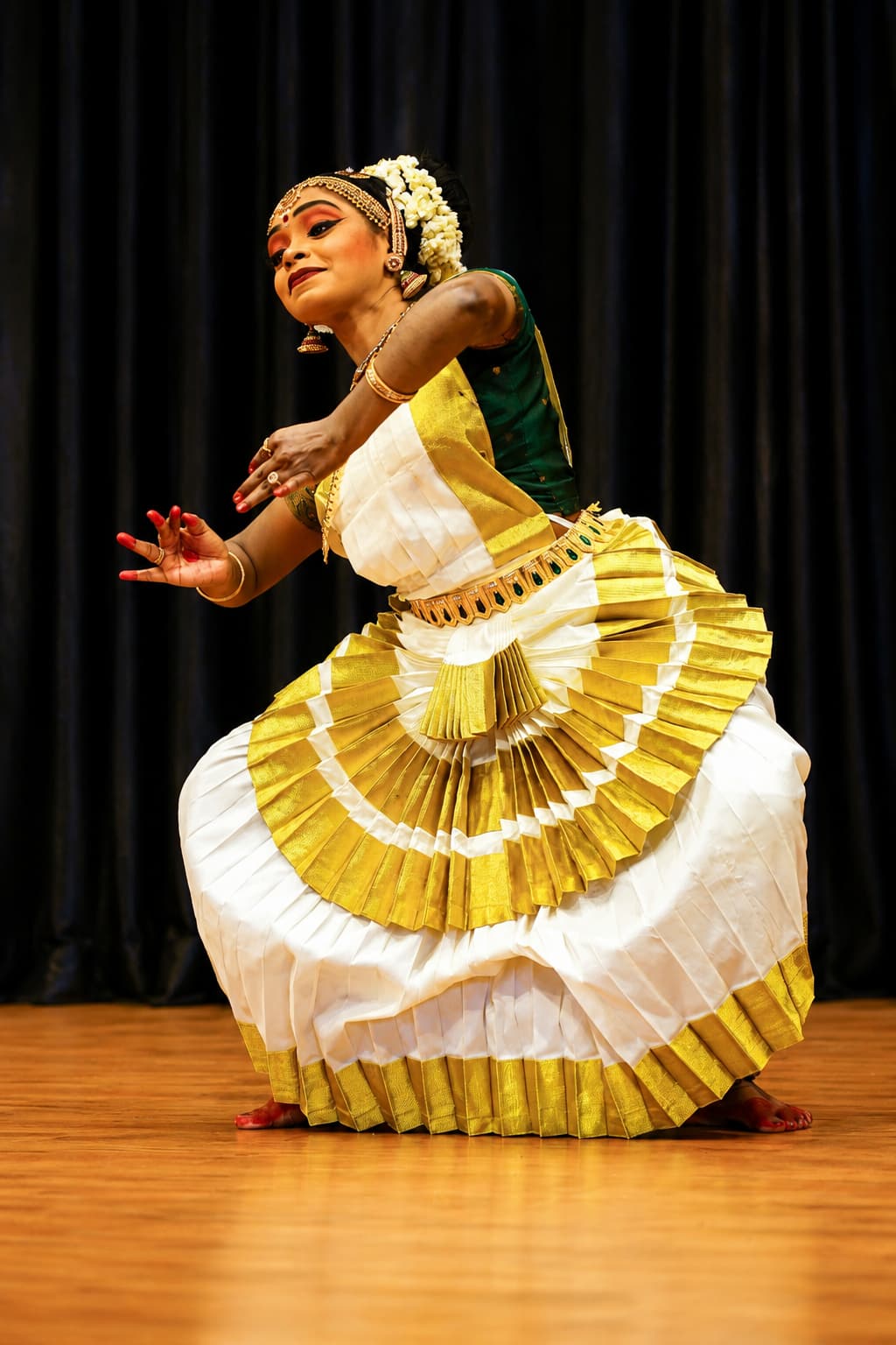 Dancer performing Mohiniyattam in a white and gold kasavu saree on stage